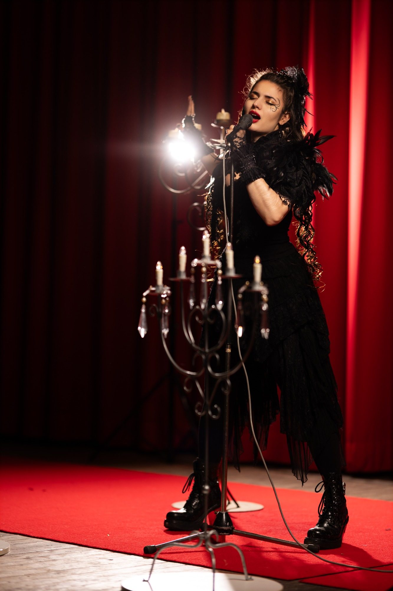 Frau mit schwarzen Kleid und Federbesatz singt vor einer Kerzenleuchterbühne.